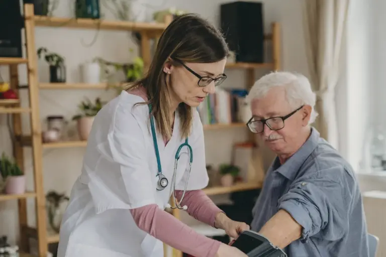 A nurse checks an older man's blood pressure at his table at home