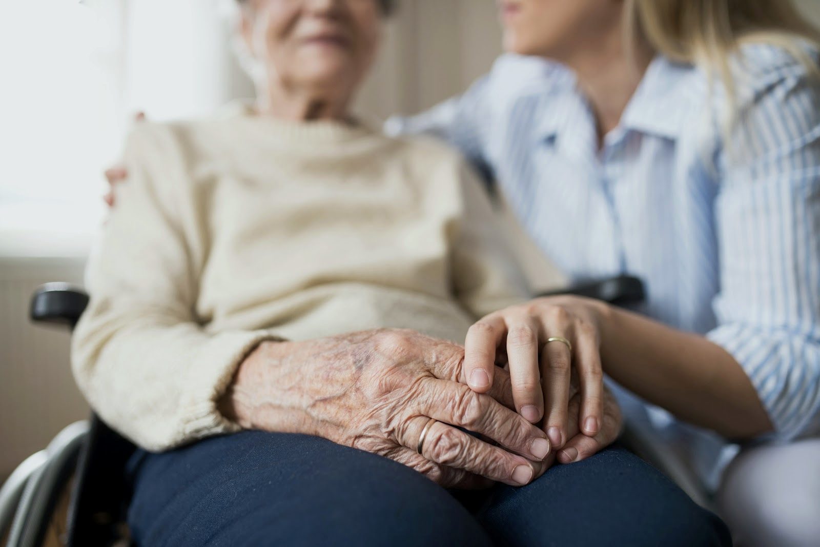 A caregiver rests a hand on an older woman’s shoulder